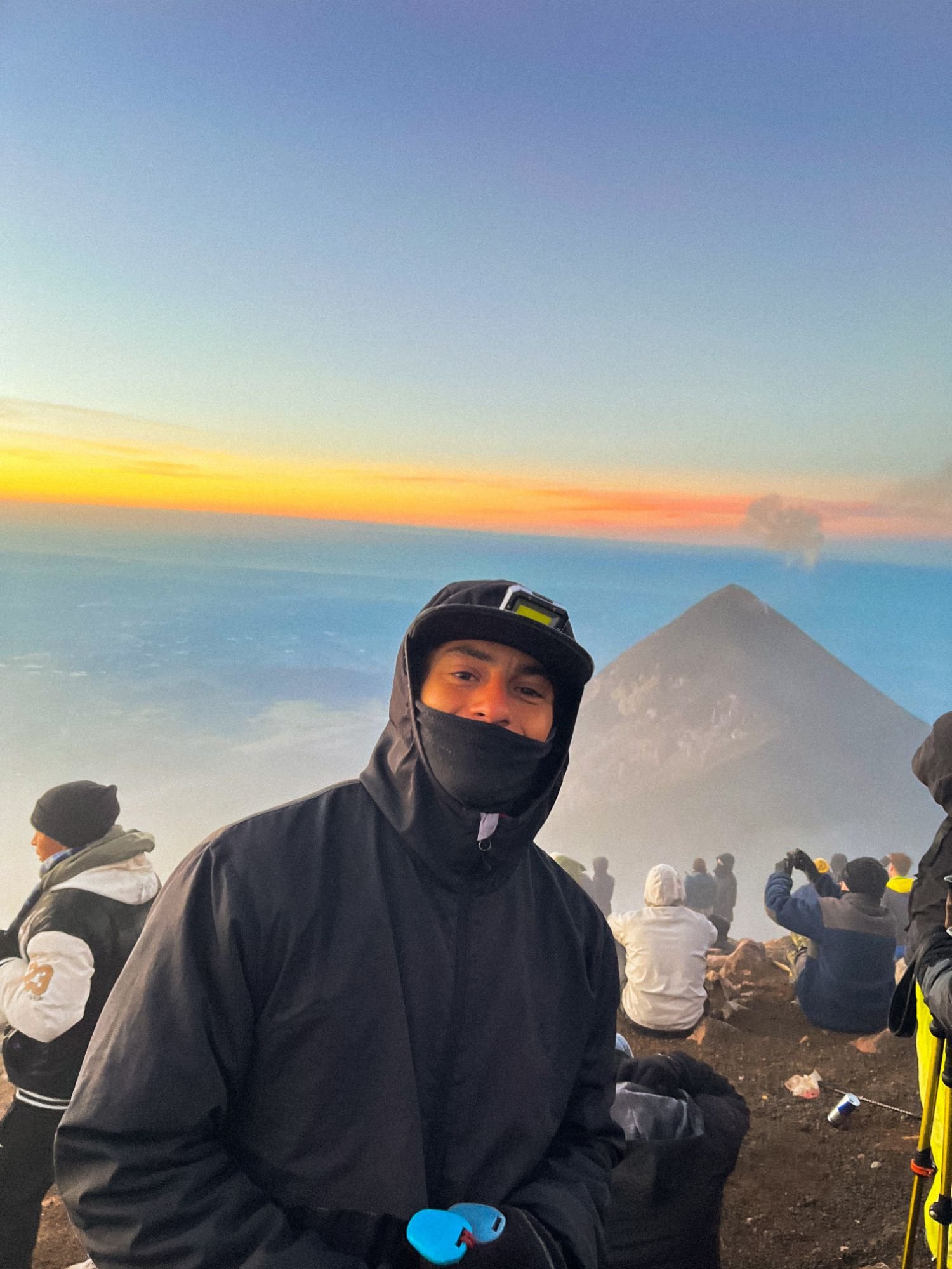 Nacho con campera y gorra en la cima de un volcán, al amanecer